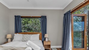 A bedroom with a wooden bed, two bedside tables with lamps, a window with curtains, and a view of greenery outside. - Hillcrest Retreat with River Views (Tweed Heads South)