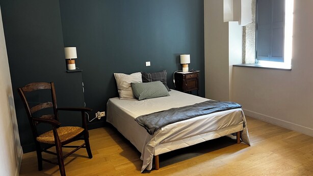 Une chambre à coucher avec un lit, deux tables de chevet, une chaise et une fenêtre.