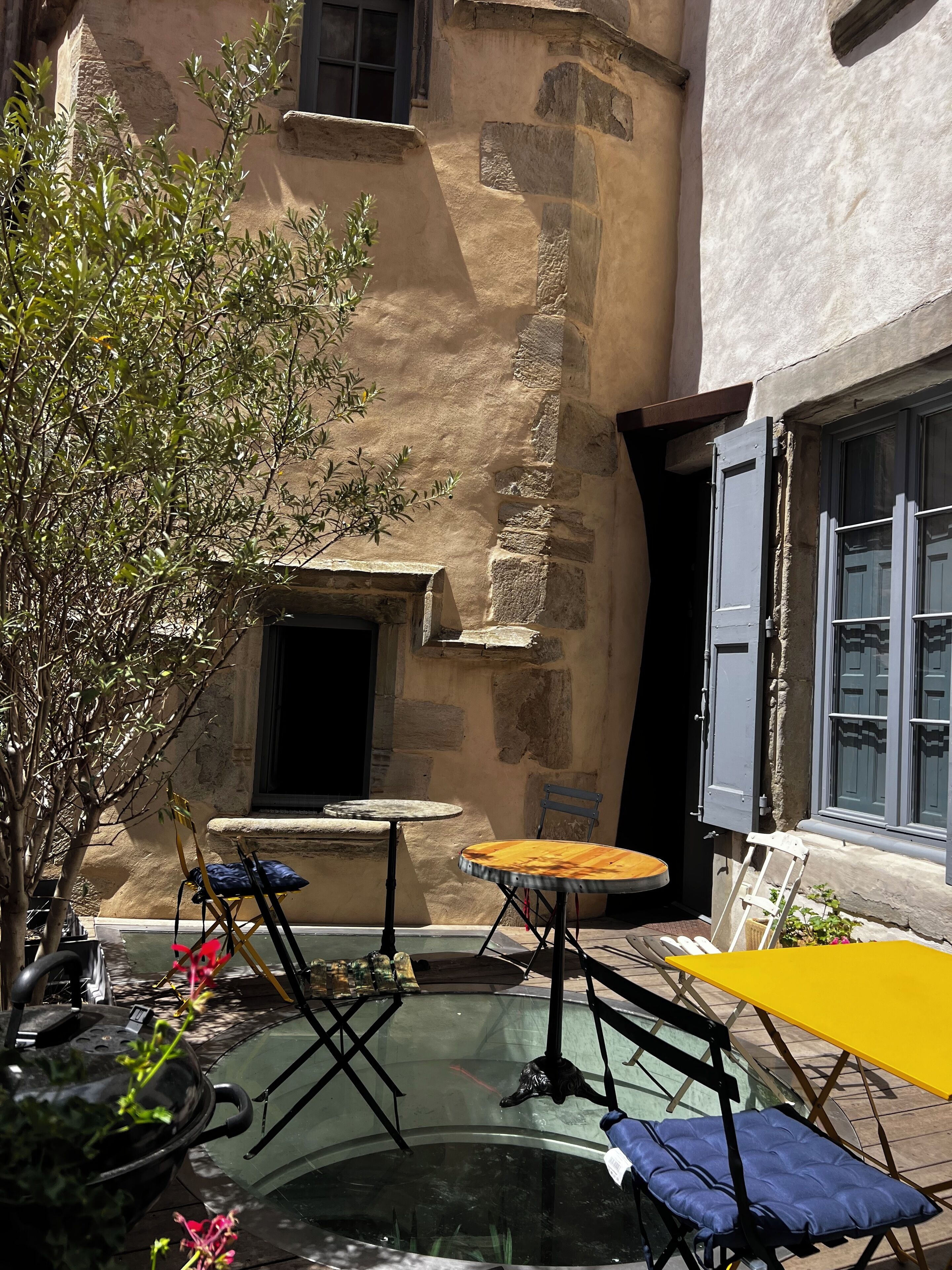 A courtyard with stone walls, a small table, a chair, and a yellow umbrella.