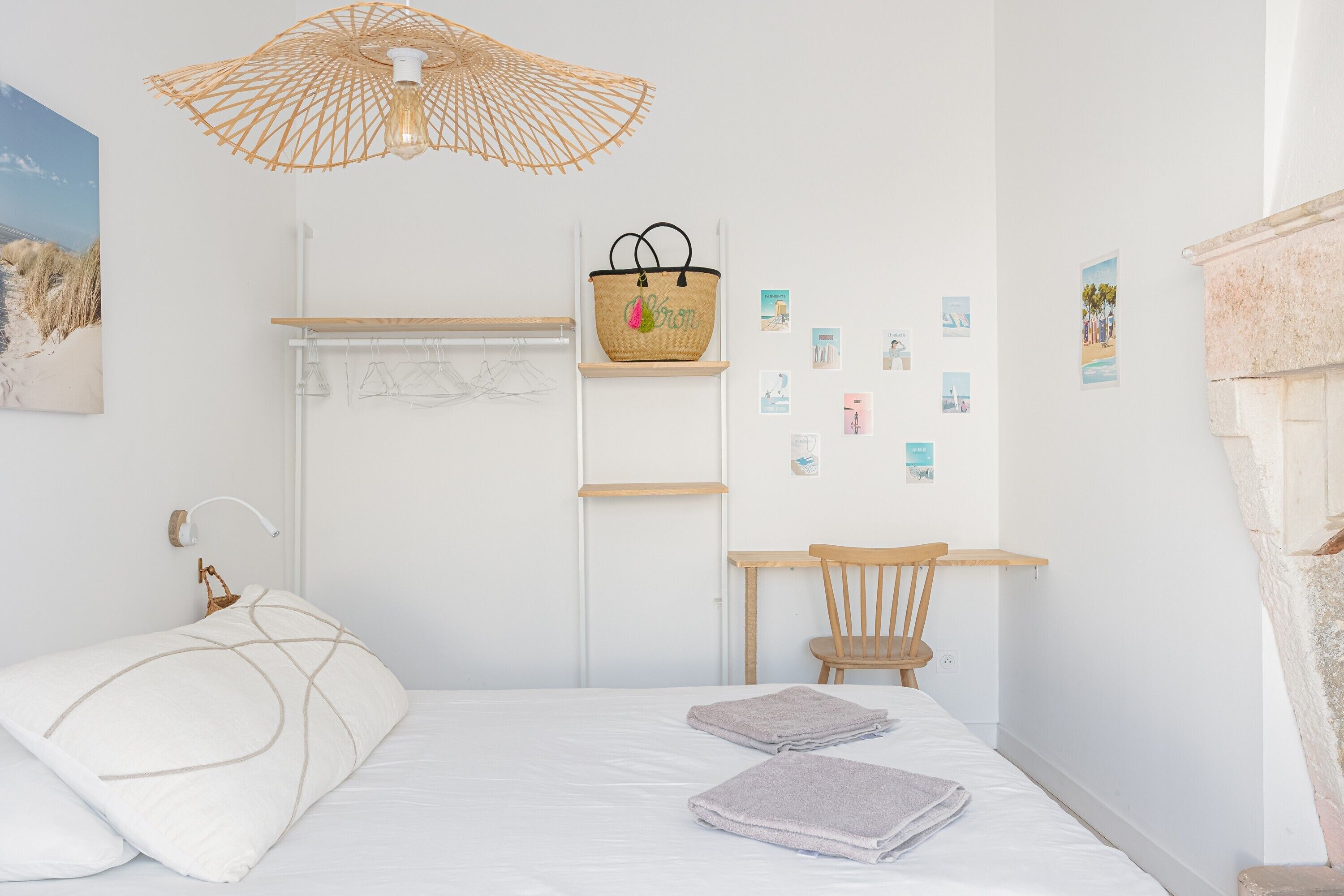 A bedroom with a bed, a desk, a chair, a hanging light fixture, and a wall-mounted basket.