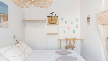 A bedroom with a bed, a desk, a chair, a hanging light fixture, and a wall-mounted basket.