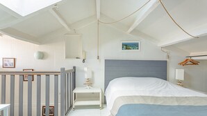 Ein Schlafzimmer mit Bett, Nachttisch, Pendelleuchte, Wandspiegel und Babybett.