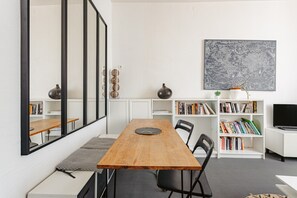 A modern dining area with a wooden table, black chairs, a large mirror, and a bookshelf with books and decorative items.