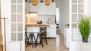 Une cuisine moderne avec des meubles blancs, un îlot central doté de tabourets et des suspensions en osier.
