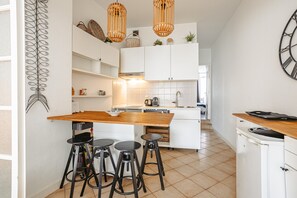 A modern kitchen with white cabinets, a wooden island with stools, and pendant lights.