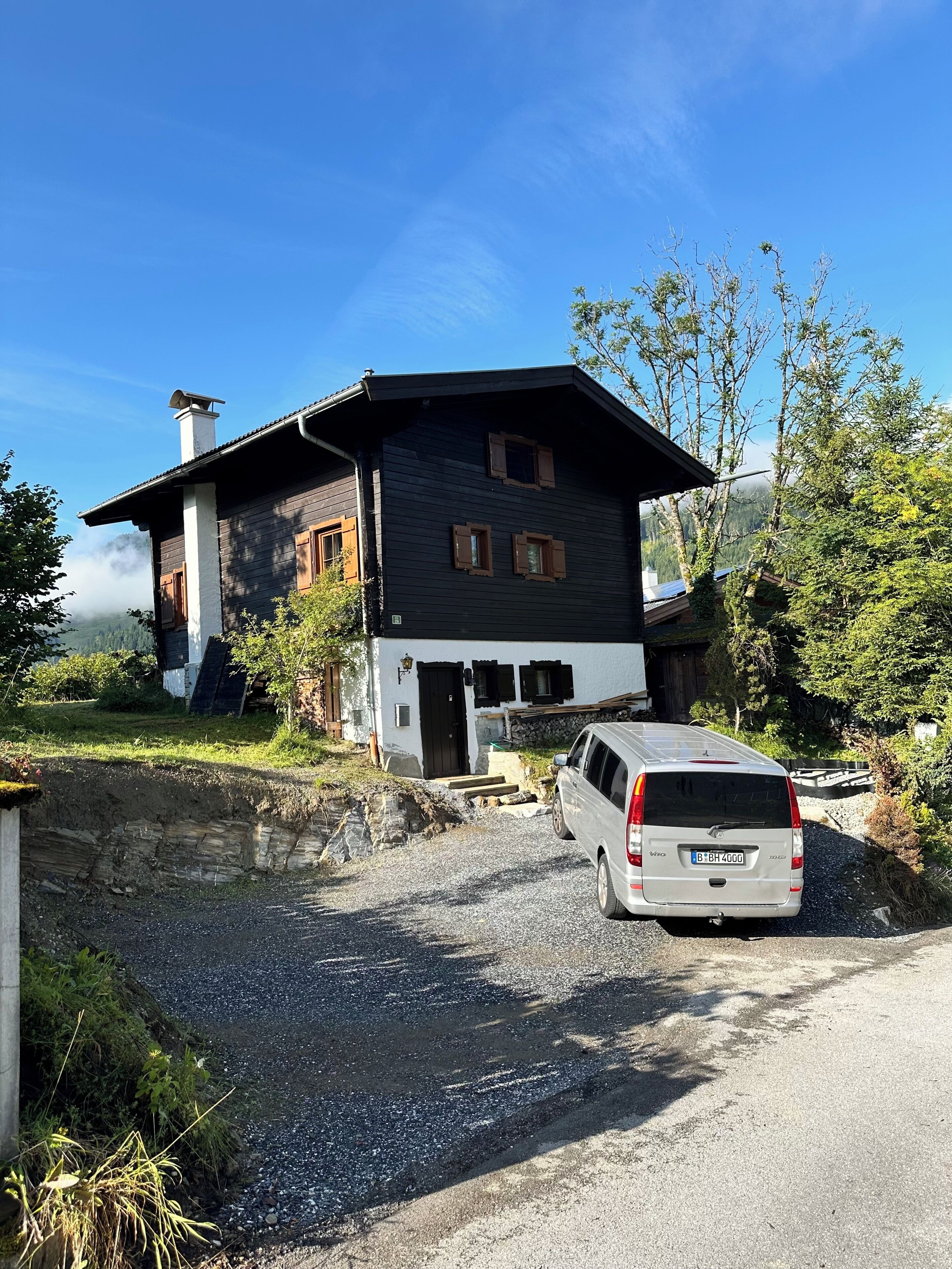 Une maison à deux étages avec une allée en gravier et un fourgon garé.