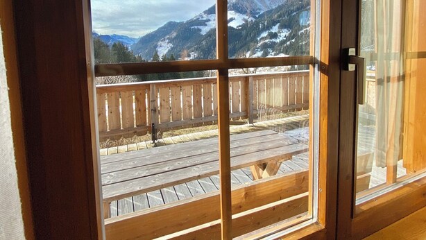 Ventana con marco de madera y vista a una terraza y montañas.