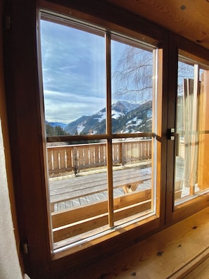 Ein Holzfenster mit Blick auf eine Terrasse und Berge.