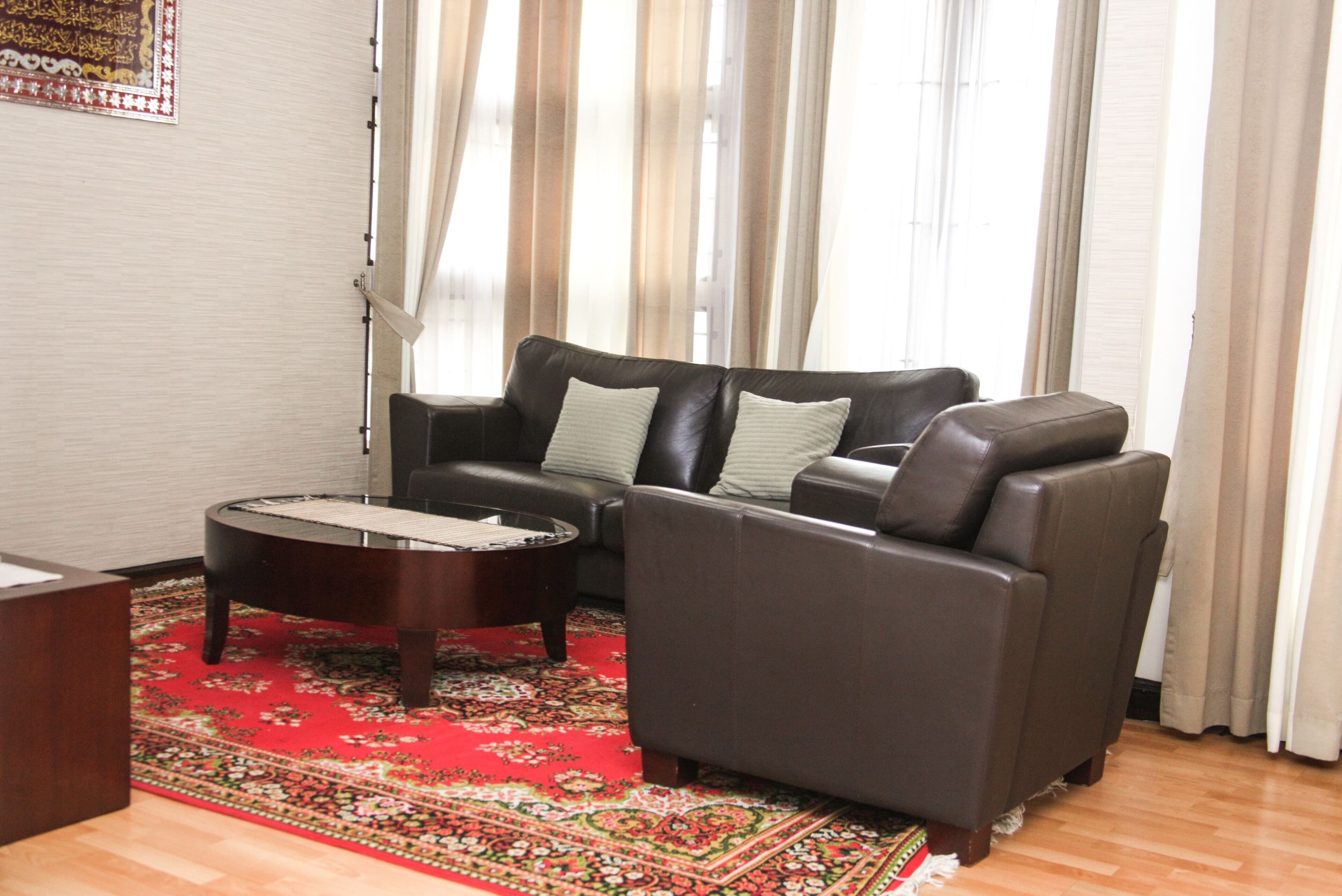 A living room with a dark brown leather sofa, a round coffee table, and a red patterned rug.