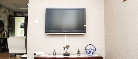 A modern living room with a mounted flat-screen TV, a wooden cabinet with decorative items, and a patterned wallpaper.