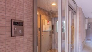 A modern elevator with a control panel, a glass door, and a visible interior of a room with a tiled floor and a door. - Sumida Midori APT (Tokyo)
