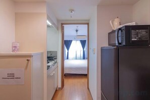 Un pasillo estrecho que conduce a un dormitorio con una cama, un refrigerador y un microondas.