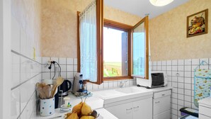Une cuisine avec des meubles blancs, une fenêtre donnant sur un beau paysage, un grille-pain et un panier de fruits.