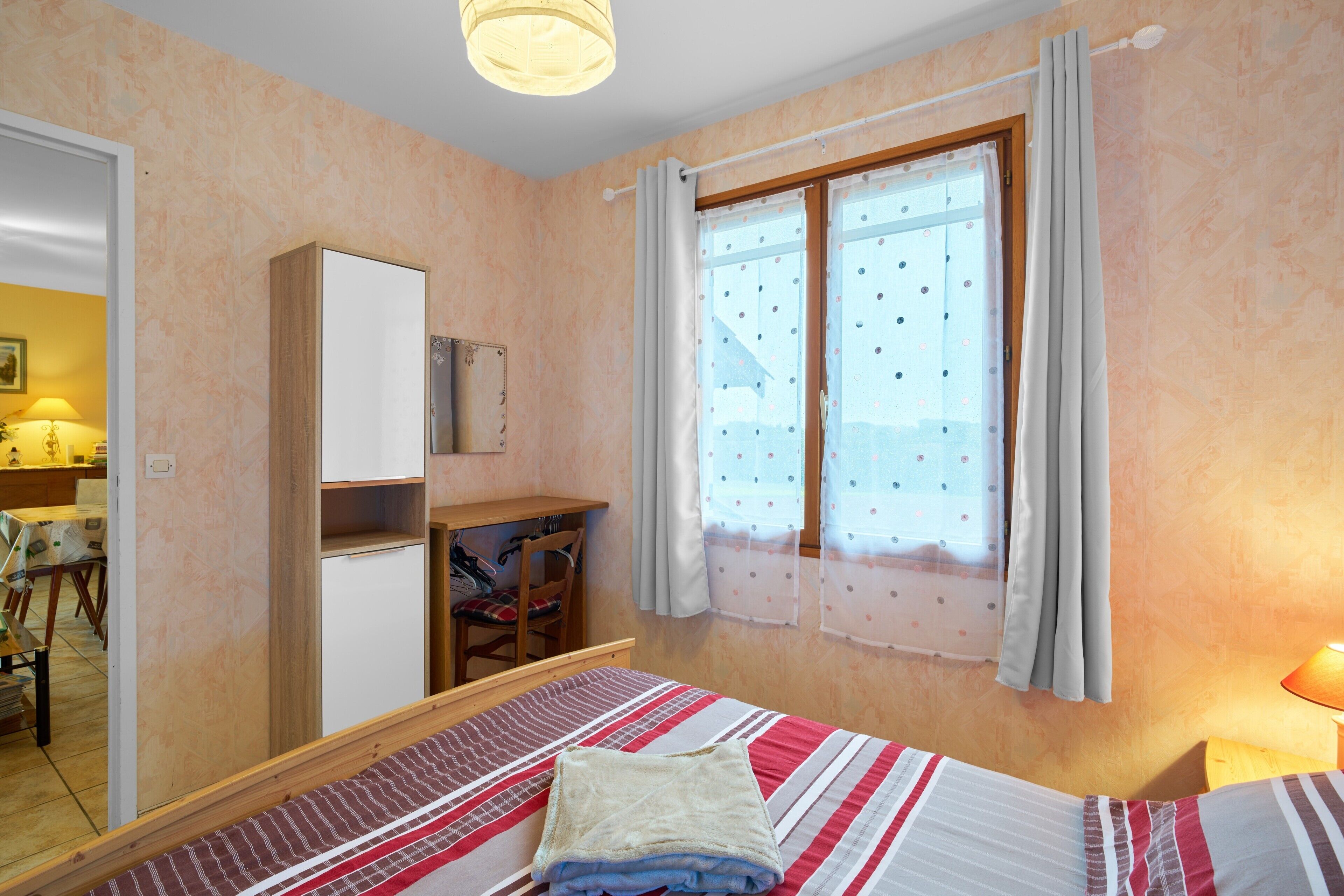 Un dormitorio con cama, escritorio, armario y ventana con cortinas.