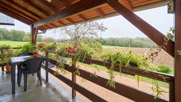 Une pergola en bois avec une pancarte indiquant « BIENVENUE », des sièges d’extérieur et des plantes en pot.
