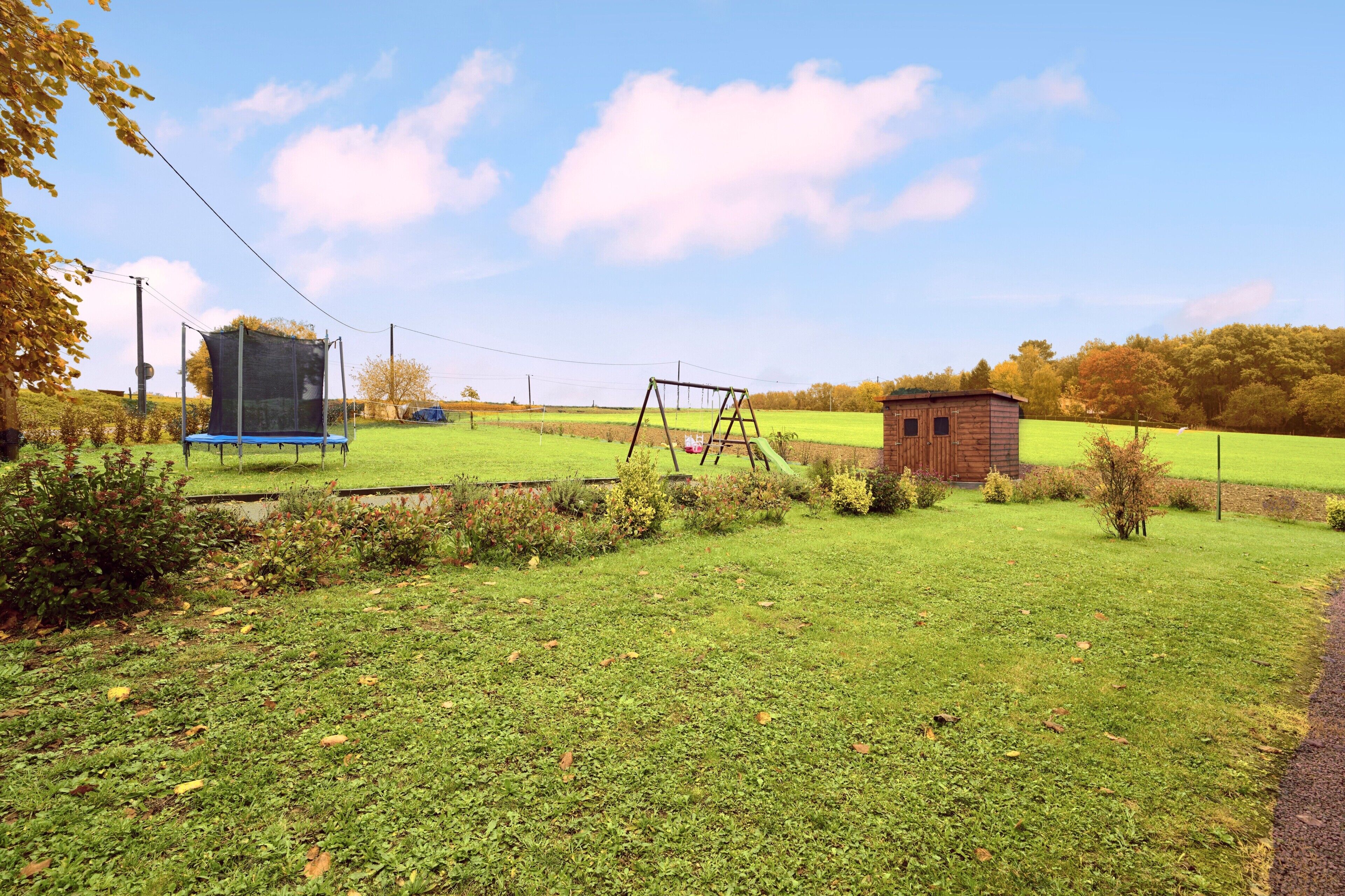 Ein grünes Feld mit Trampolin, Schaukeln und einer kleinen Holzhütte.