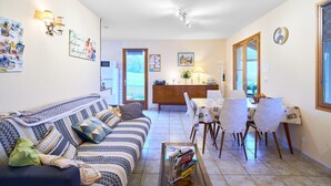 Un salon chaleureux avec un canapé, une table à manger et des chaises, et un coin cuisine à l’arrière-plan.