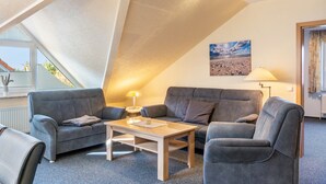 Un salon moderne avec un plafond en pente, des canapés gris, une table basse en bois et un tableau représentant un paysage accroché au mur.