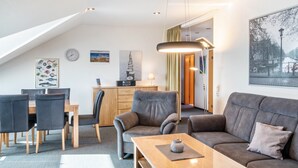 A modern living room with a dining area, a gray sofa, a wooden coffee table, and a ceiling with a skylight. - Apartment 'Kirschner's 2' with Shared Terrace and Wi-Fi (Horumersiel-Schillig)