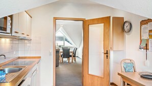A modern kitchen with a built-in microwave, a sink, and a dining area with a table and chairs. - Apartment 'Kirschner's 2' with Shared Terrace and Wi-Fi (Horumersiel-Schillig)