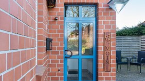 A brick building with a blue door, a wooden sign with 'MOIN' on it, and a small outdoor seating area with chairs. - Apartment 'Kirschner's 2' with Shared Terrace and Wi-Fi (Horumersiel-Schillig)