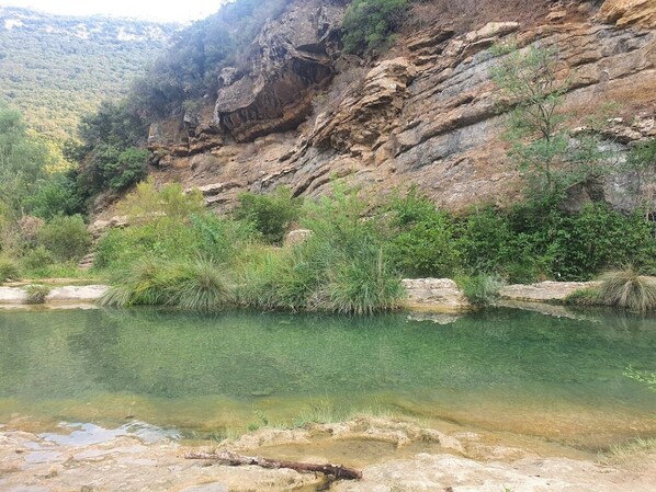 A natural landscape with a clear water body surrounded by rocky terrain and vegetation. - Ostal de la placette (Padern)