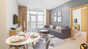 Een moderne woonkamer met een grijze bank, een eettafel voor twee personen en een groot raam met uitzicht op de stad.