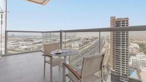 Een balkon met een tafel en stoelen, met uitzicht op een stadsgezicht met gebouwen en een snelweg.