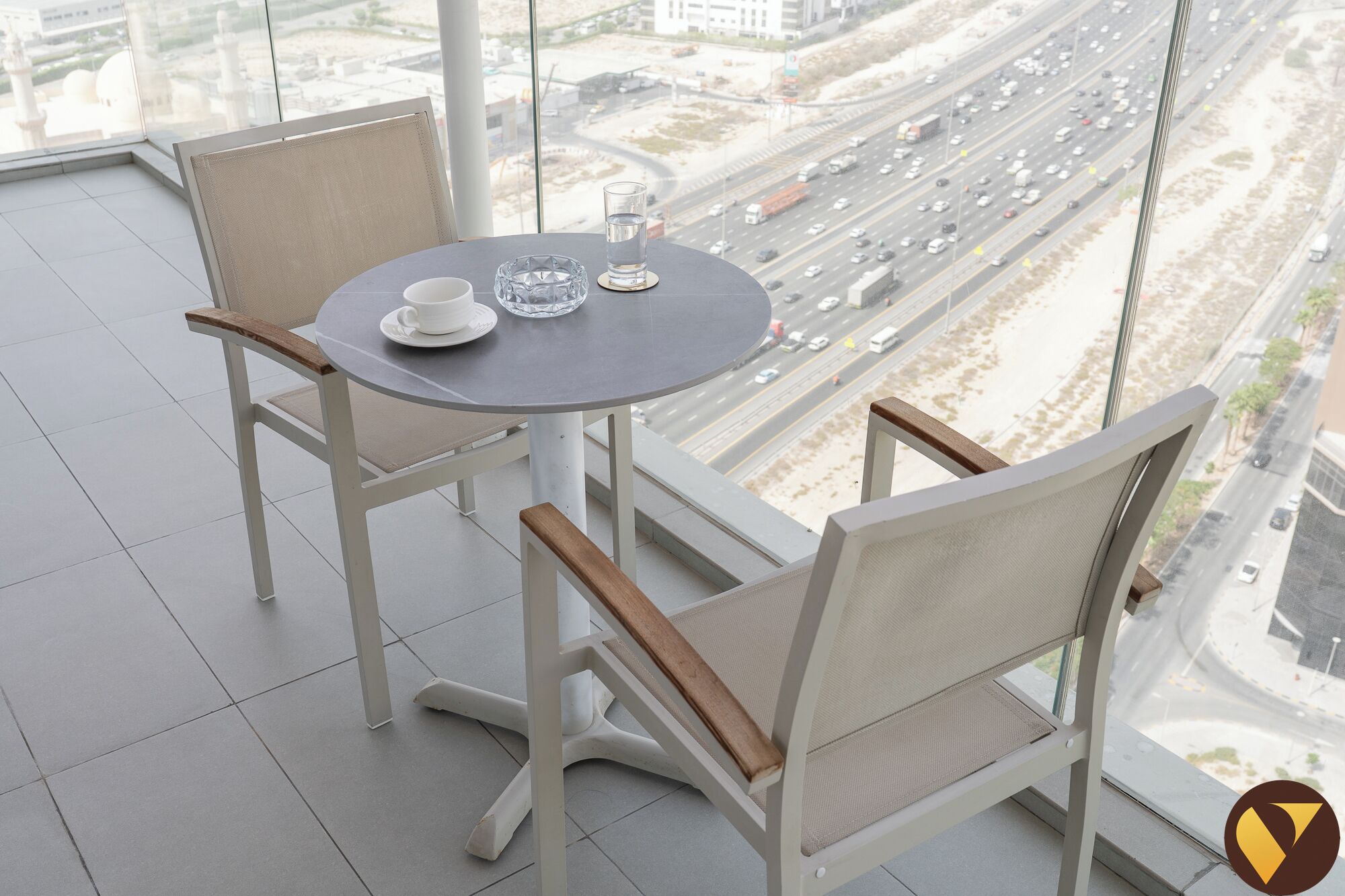 A balcony with a round table, two chairs, a glass, and a cup.