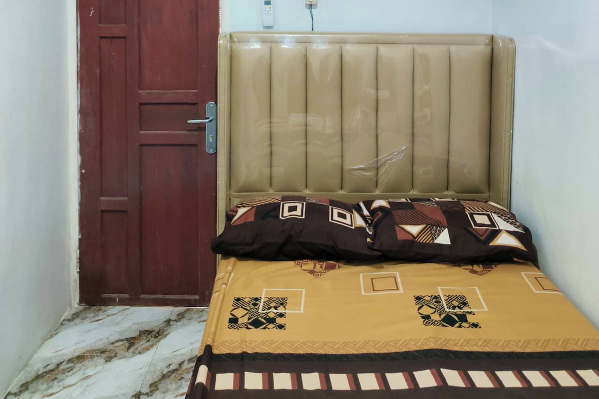 Una habitación pequeña y poco amueblada, con una cama individual, una puerta de madera y un equipo de aire acondicionado.