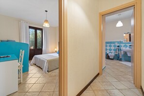 A hotel room with a bed, a desk, a chair, a window with curtains, a hanging light fixture, and a bathroom with a sink and mirror. - Casa di Lisa Villasimius (Villasimius)