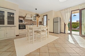 A kitchen with a dining table, chairs, a refrigerator, and a view through the glass door. - Casa di Lisa Villasimius (Villasimius)