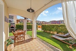 A covered patio with a table and chairs, a lounge chair, and a view of a residential area. - Casa di Lisa Villasimius (Villasimius)