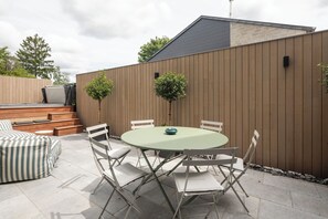 Un patio con una mesa redonda y sillas, un sofá a rayas y una valla de madera.