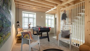 A room with a foosball table, a white chair, a colorful cushion, and a large abstract painting. - 3 bedroom house with Jacuzzi (Hotton)