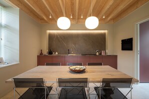 Un comedor moderno con una mesa de madera, sillas de malla negra, un salpicadero de mármol e iluminación colgante.