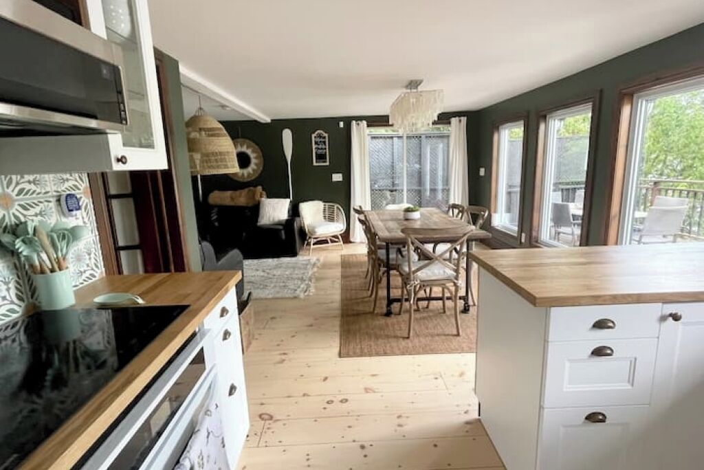 Una cocina con encimera de madera, un comedor con mesa y sillas, y vistas amplias a través de grandes ventanales.