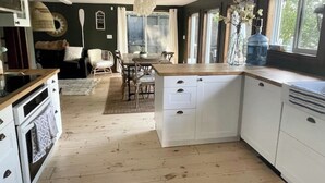 A kitchen with white cabinets, a wooden countertop, and a dining area with chairs and a table. - Muskoka Cabana - Sandy beach cottage in Muskoka (Utterson)