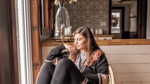 A person sitting on a wicker chair in a room with a patterned wall and a wooden counter. - Muskoka Cabana - Sandy beach cottage in Muskoka (Utterson)