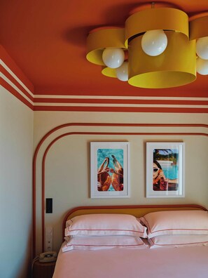 Une chambre d’hôtel avec un lit, une table de chevet, un téléphone et deux tableaux encadrés au mur.