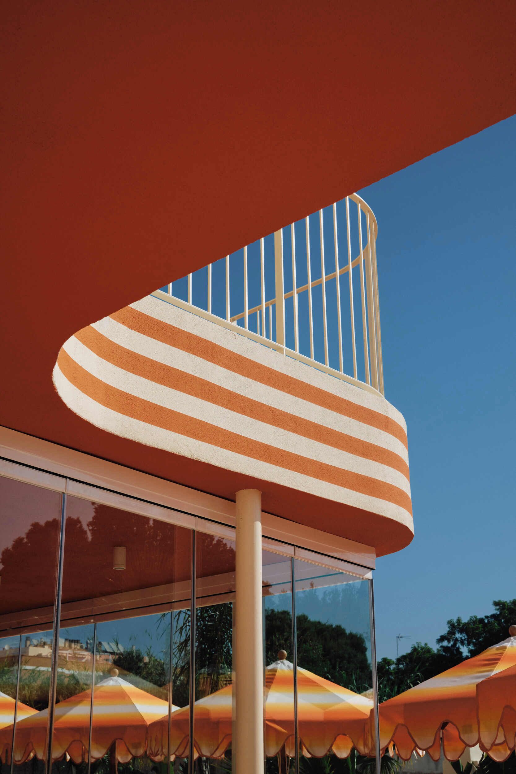 Un edificio con estructura curva, fachada de vidrio y toldo a rayas.