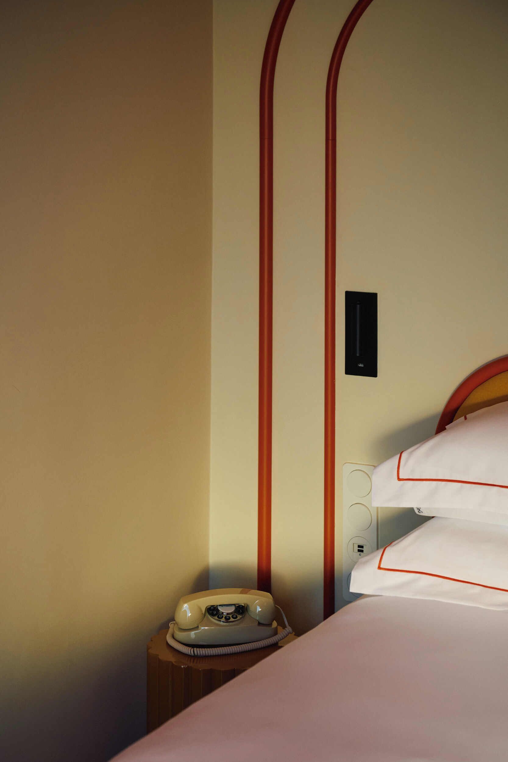 A hotel room with a bed, a bedside telephone, and a wall socket.