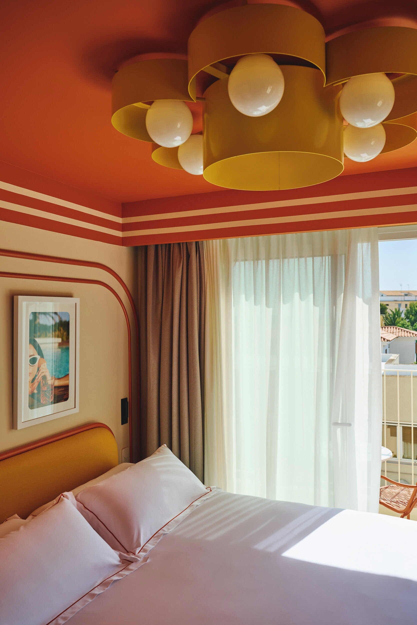 Une chambre d’hôtel avec un lit, des rideaux, un tableau encadré et un balcon doté d’une balustrade.