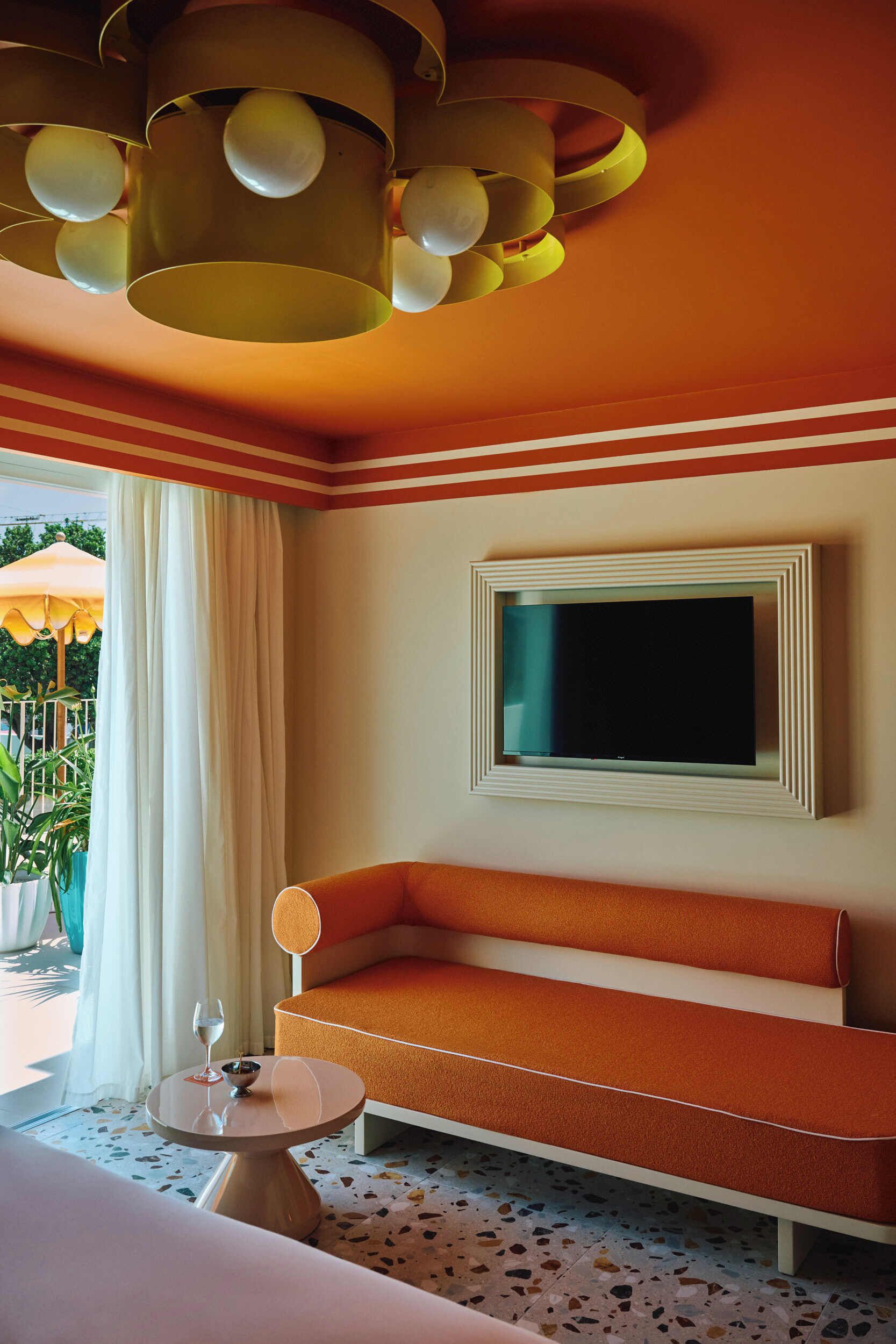 Una habitación con sofá, televisor montado en la pared, una mesa redonda con una copa de vino, y una lámpara en el techo.
