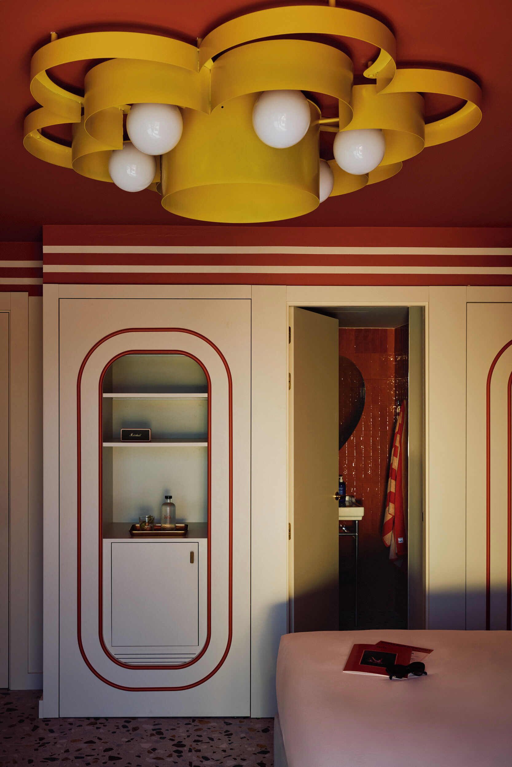 Habitación de hotel con cama, armario con espejo, puerta que da a un baño y una lámpara de techo amarilla única.