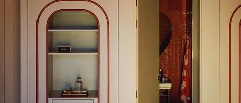 A hotel room with a bed, a wardrobe with a mirror, a door leading to a bathroom, and a unique yellow ceiling light fixture.