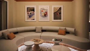 A modern lounge area with a curved sofa, a small round table, and three framed photographs on the wall. - Riviera Hotel Menorca  (Ciutadella de Menorca)