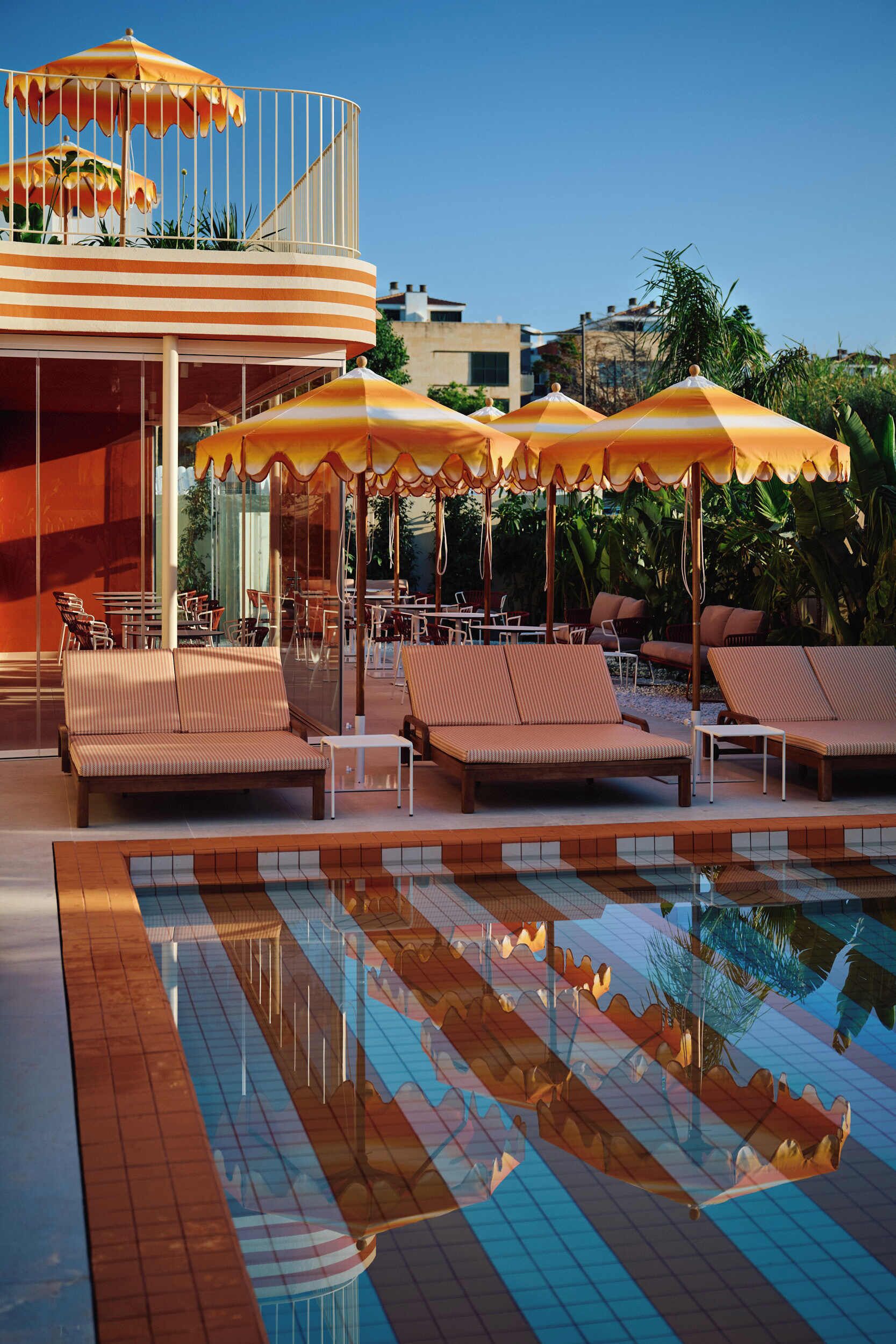 A pool area with lounge chairs and umbrellas, a covered seating area, and a reflection pool.