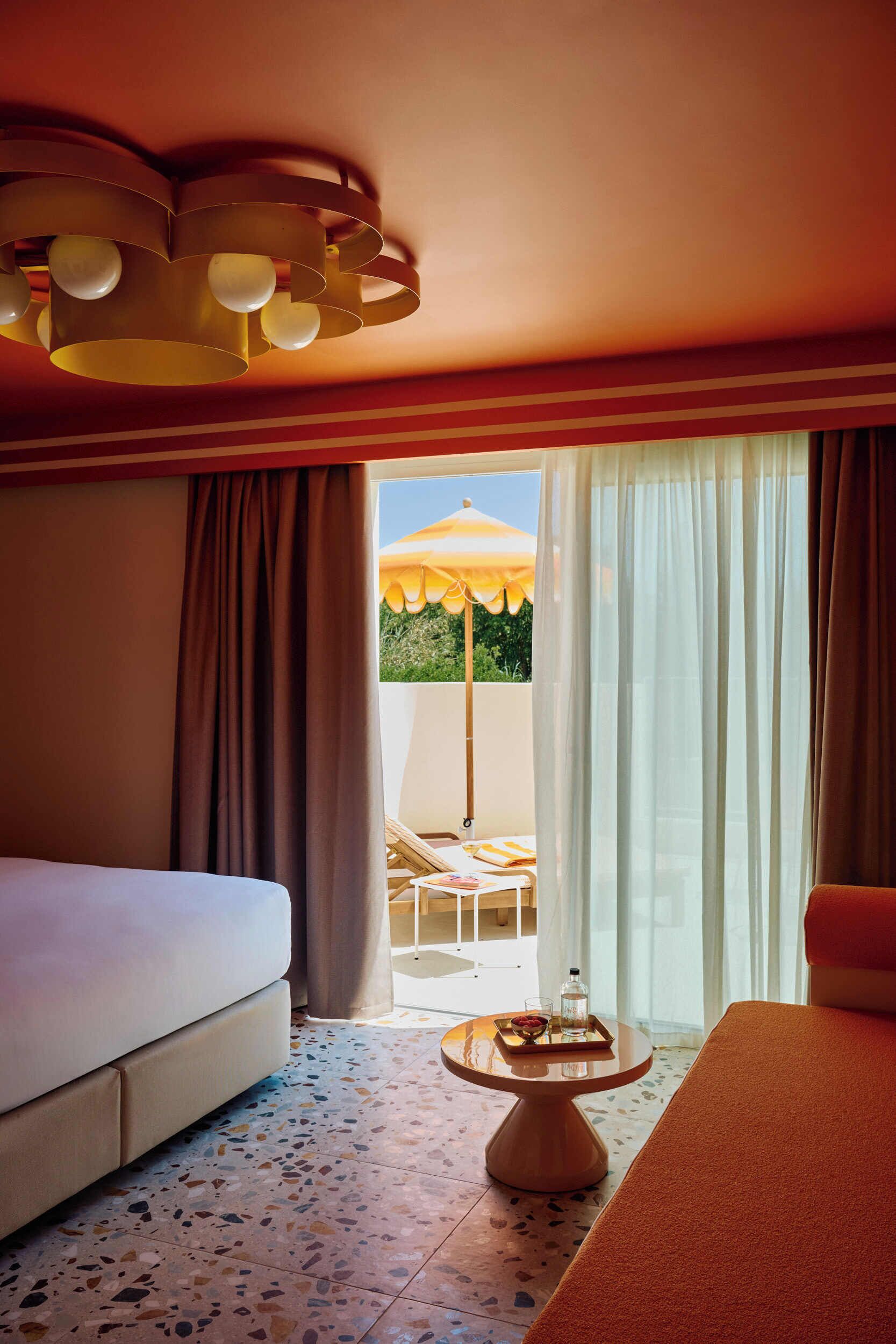 Habitación de hotel con una cama, una mesita con bandeja, una silla y vista a un espacio exterior con sombrilla.