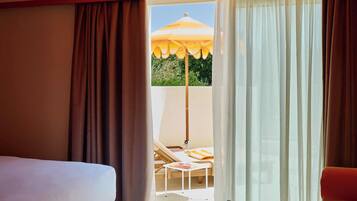 Habitación de hotel con una cama, una mesita con bandeja, una silla y vista a un espacio exterior con sombrilla.